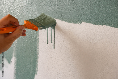 Repairman painting white wall in apartment green using brush, closeup
