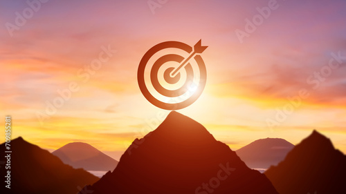 Silhouette target dartboard achievement concept with bullseye on mountain peak at sunrise.