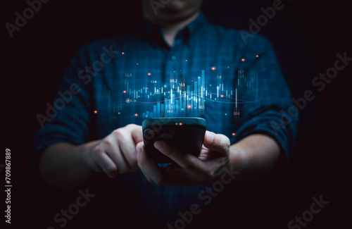 Businessman holding smartphone with virtual technical graph and chart for analysis stock market, trader use technology invest and value investment concept.