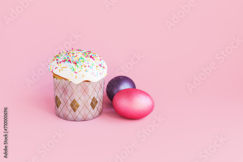 Traditional russian Easter ortodox cake with daffodil flower and colorful eggs on light pink background. Kulic, Kulich, Paska homemade bread with glaze. Spring christian holiday. Festive celebration