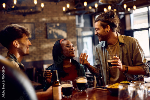 Happy black woman and her friend talking and drinking beer in pub.