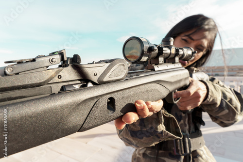 Rifle with an optical sight in the hands of a black African woman in military uniform, aiming at the optical sight while keeping her finger on the trigger of the rifle.Military action,sniper shooting