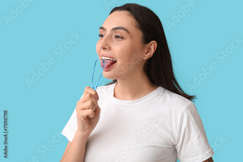 Young woman using tongue scraper on blue background, closeup