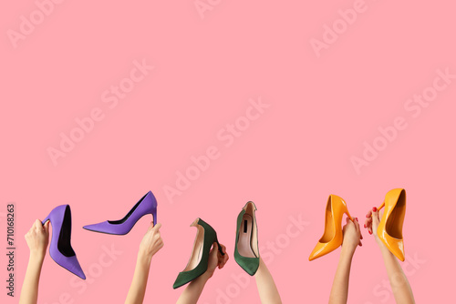 Female hands holding different stylish shoes on pink background