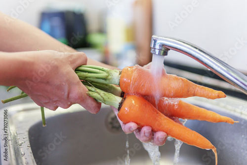 Woman hands washing fresh orange carrots in a kitchen