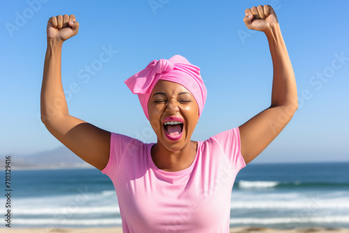 Exuberant woman with raised arms celebrating on seashore. Concept of cancer awareness.