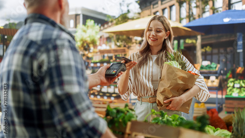 Modern Female Shopper Using Smartphone with Contactless Payment Technology to Pay for Organic Vegetables at a Farmers Market. Street Vendor Holding an Electronic Online Payment Terminal Device