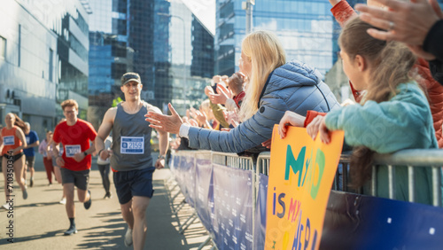 Marathon Audience Supporting and Cheering Their Loved Ones Participating in the Race: Athletic Male Marathon Runner Giving a High Five to Female Family Member in the Audience While Running