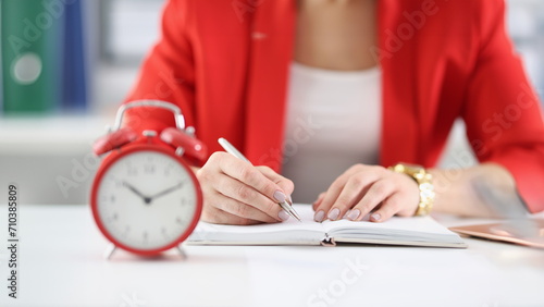 Businesswoman makes notes in documents there is an alarm clock next to it. Time tracking and employee deadlines concept
