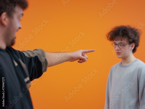 A man is pointing at a boy with glasses using his hand and index finger, mocking him, laughing at him, blaming and accusing him. The accused teen looks bullied, harrassed, tired, fed up or ashamed.