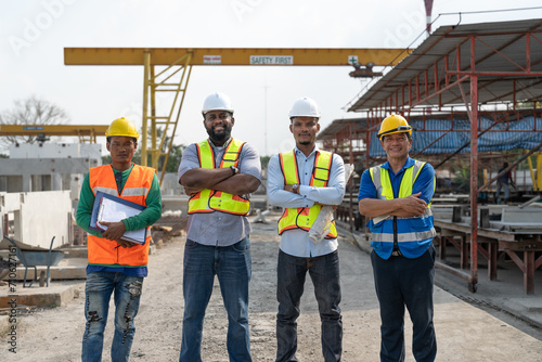 Group of diverse teamwork civil engineers foreman and workers wear safety vests with helmets standing and crossed arm at construction site factory produce precast concrete