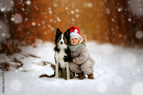 Mała dziewczynka z czapką Mikołaja przytula psa rasy border collie