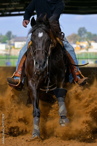 A close up view of a rider sliding the horse in the dirt 