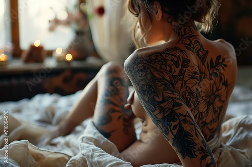 Sexy beautiful young slender woman with a tattoo on her back sitting on bed. Back view of an erotic blonde in bedroom