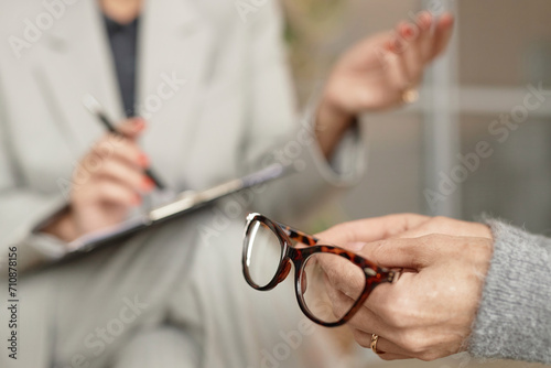 Detail shot of unrecognizable senior woman holding glasses in hand during consultation with doctor or therapist, copy space