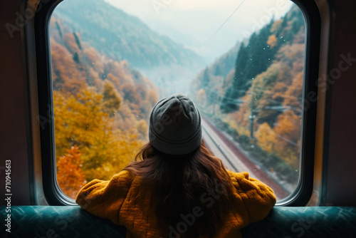 A cinematic and symmetrical beautiful shot of a female traveler, travel blogger and inspirational adventurer looking out of the train window, looking at the amazing landscape of the autumn mountains