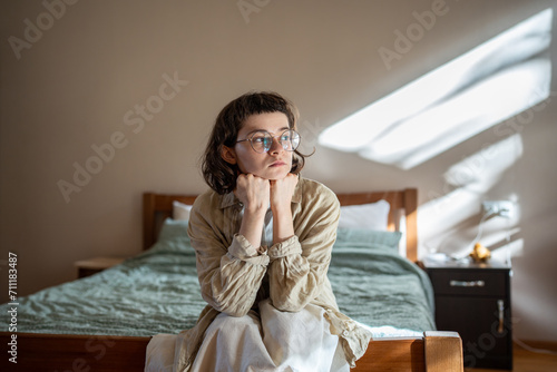 Depressed lonely woman sitting on cozy bed sadly look at window feeling anxiety. Alone girl suffering from emotional pain having life troubles, problems. Mental disorder anhedonia, stress discomfort