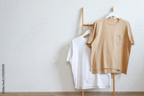 Blank white and brown t-shirt mockup on hanger displayed on a wooden clothes rack