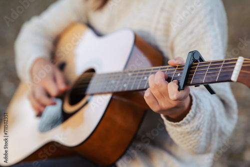 Guitar in hands of a young woman playing it. Playing music outdoors, using equipment capo