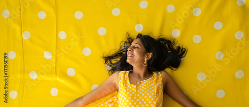 Mulher indiana feliz deitada em um tapete amarelo com bolinhas brancas