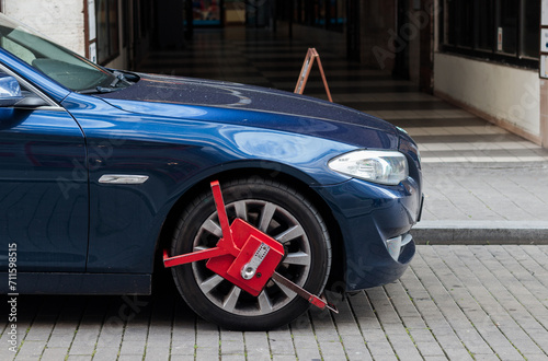 Red colored wheel clamp (wheel boot, parking boot) installed on a luxury car by police for law enforcement and parking violation in Czech Republic
