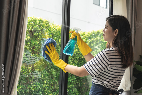Young Asian housewife wearing yellow gloves holding professional home window glass cleaning spray.