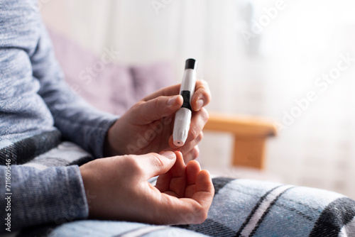 Middle age caucasian man sitting on the sofa pierced his finger with lancet for home glucose test. Diabetes awareness mockup with copy-space.