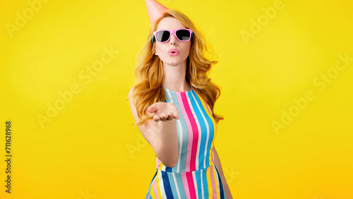 Wink, flirt and hipster woman sending air kiss and happy excited smiling. Fashionable lady blowing a kiss with confidence flirty emotion for cosmetics makeup, trendy outfit in studio yellow background