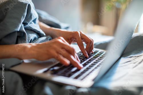 Close up hands of woman typing on laptop keyboard in bed