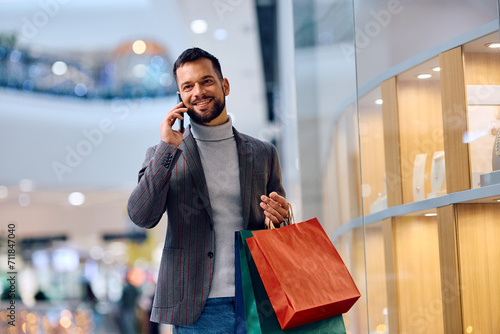 Young happy man communicating over mobile phone while buying in shopping mall.