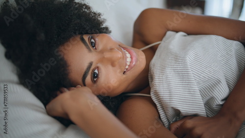 Happy lady wakeup bedroom portrait. African woman looking camera lying bed alone