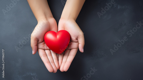 Top view photo of hands holding red heart on black background, healthcare, love, organ donation, mindfulness, wellbeing, family insurance and CSR concept, World Heart Day.