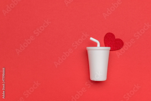 A white drink glass with a tube and a red heart on a red background.