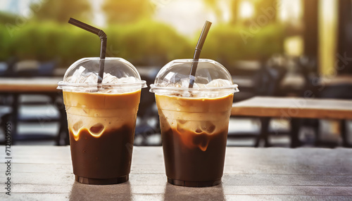 Plastic takeaway cups of delicious iced coffee on table in outdoor cafe with blurry background