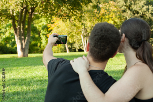 Pareja haciendose un selfie en el cesped del parque. Espalda de un selfie