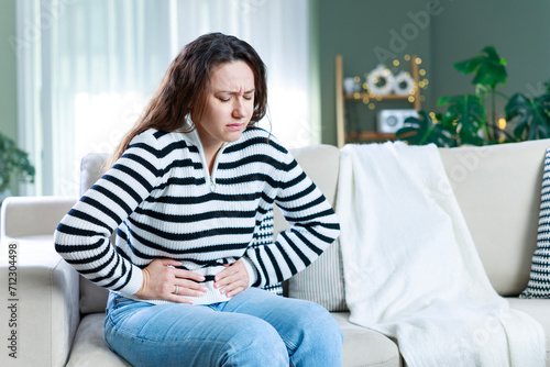 Young woman sitting on the couch at home with a pain in her stomach