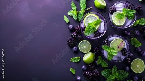  two glasses of mojito with limes, blackberries, and mints on a dark purple background.