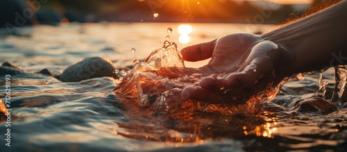 Hand touching water in river at sunset, summer