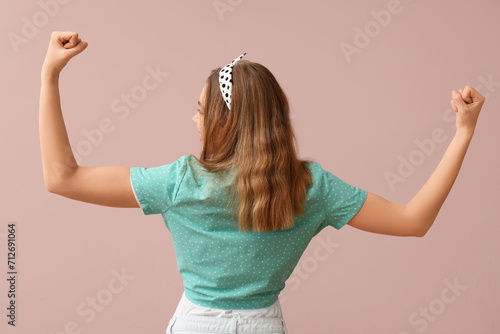 Happy young pin-up woman showing her muscles on pink background, back view