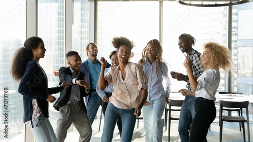 Corporate party. Overjoyed group of multicultural students employees dancing in modern office having fun achieving success in teamwork. Excited mixed race colleagues friends celebrate business reward