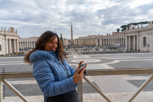happy middle aged female tourist using mobile phone in front of san pietro square in rome