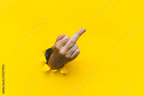 Middle finger of right hand, insulting gesture. Torn hole in yellow paper. Fuck you concept. Aggressive reaction.