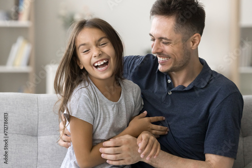 Cheerful loving daddy tickling excited shouting daughter kid, laughing, having fun at home with child, enjoying fatherhood, playtime. Happy girl playing active games with dad