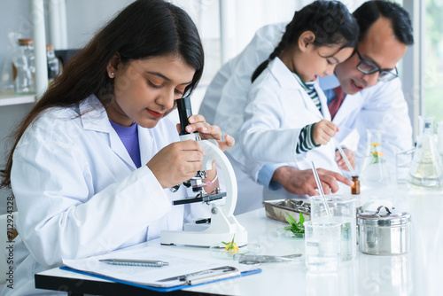 Indian scientist woman student using microscope do an experiment at biology class in school laboratory while teacher teaching another kid student. Education, science and school concept