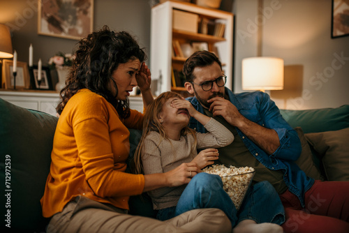 Parents and daughter immersed in a film, creating cherished memories with a bowl of popcorn