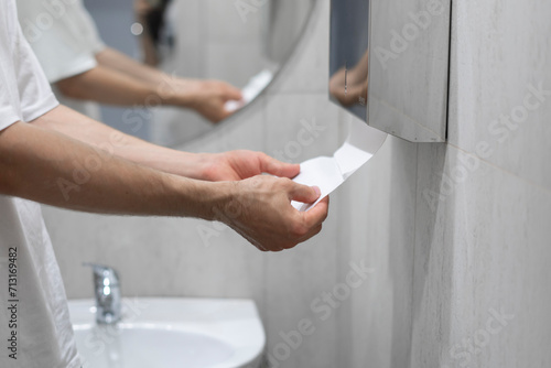 A person is captured drying their hands using a paper towel in the clean and well-lit confines of a modern bathroom setting.