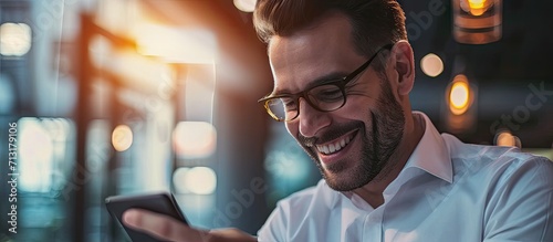 Happy dark skinned man in white shirt laughing while using cellphone device for checking business news on website cheerful male employee in classic glasses browsing wireless internet via mobile