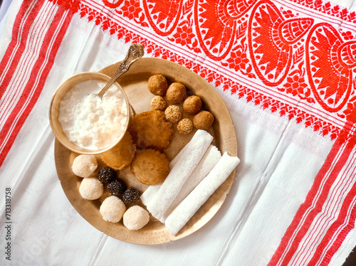 Assamese traditional food items like pitha, laddu, doi sira with assamese gamosa background with japi motifs