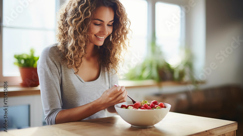 Athletic woman eating a healthy bowl of muesli with fruit sitting on floor in the kitchen at home 