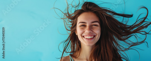 Smiling young pretty woman with brunette brown long groomed hair isolated on flat blue background with copy space. Perfect hair care products banner template, hair salon.
